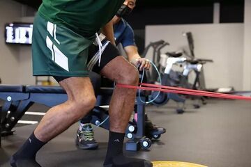 Person doing resistance band leg exercise in a gym, with red bands stretched around the legs.