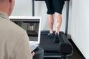 Physical therapy assessment with leg markers on a person walking on a treadmill as a clinician observes from a laptop