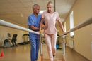 Therapist assisting a patient walking with parallel bars in a rehab gym