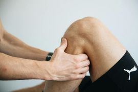 Hands massaging a bent knee, suggesting a sports injury or knee pain exercise