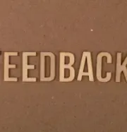 3D letters spelling “FEEDBACK” on a brown textured wall.