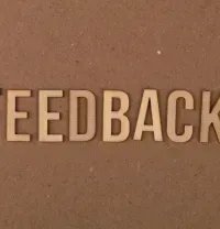 3D letters spelling “FEEDBACK” on a brown textured wall.