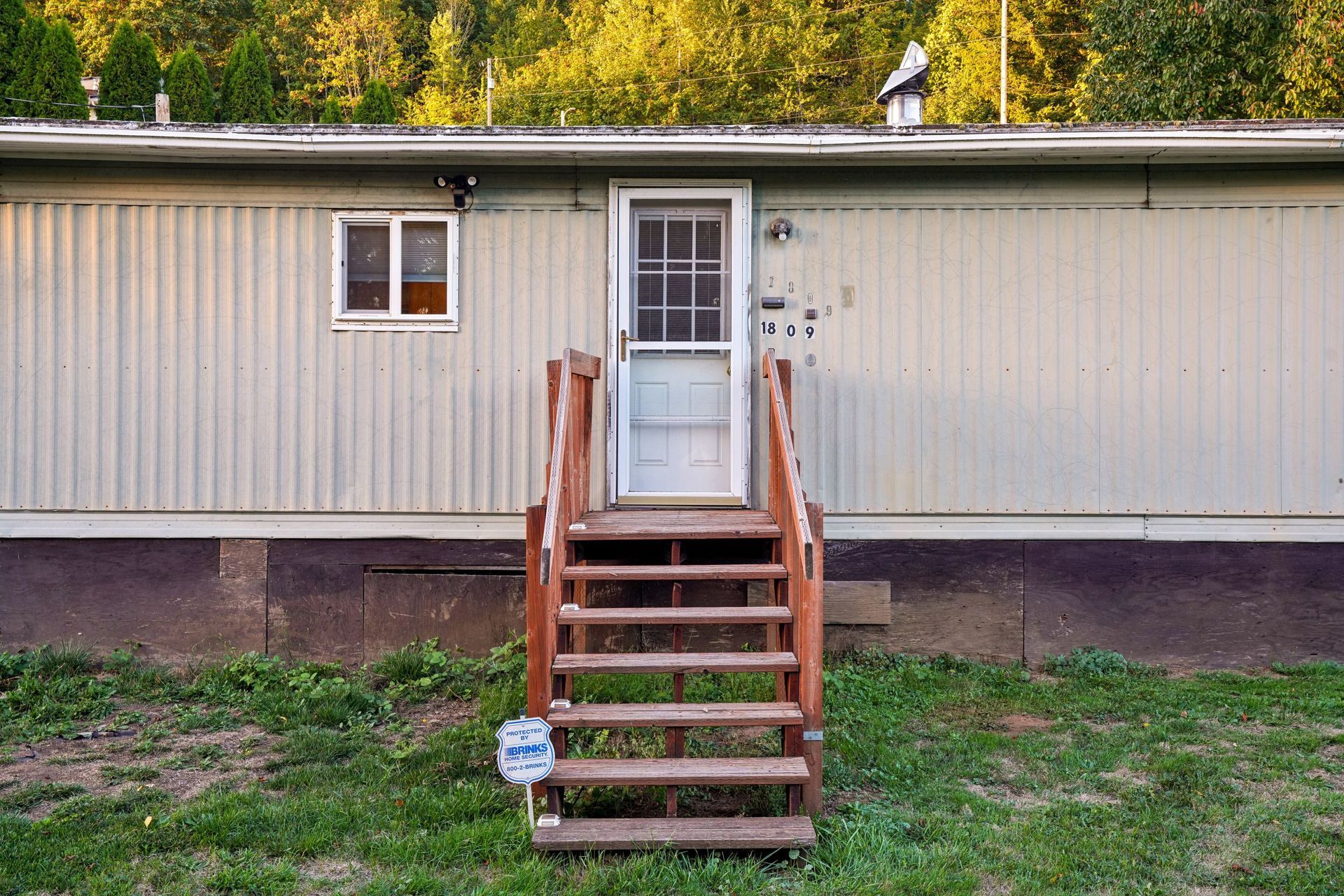 Front of a beige mobile home with a central wooden staircase, white door, and grassy yard.