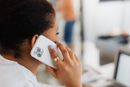 Person holding a white smartphone to their ear in a bright office setting