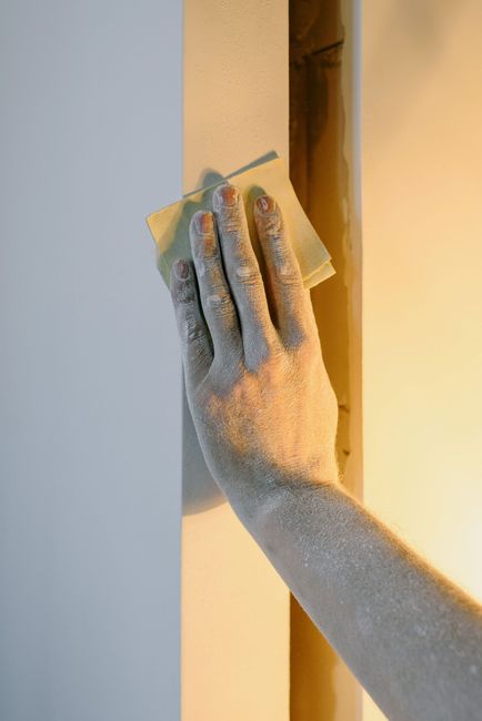 Hand wiping a white wall with a cloth near a doorway in warm light