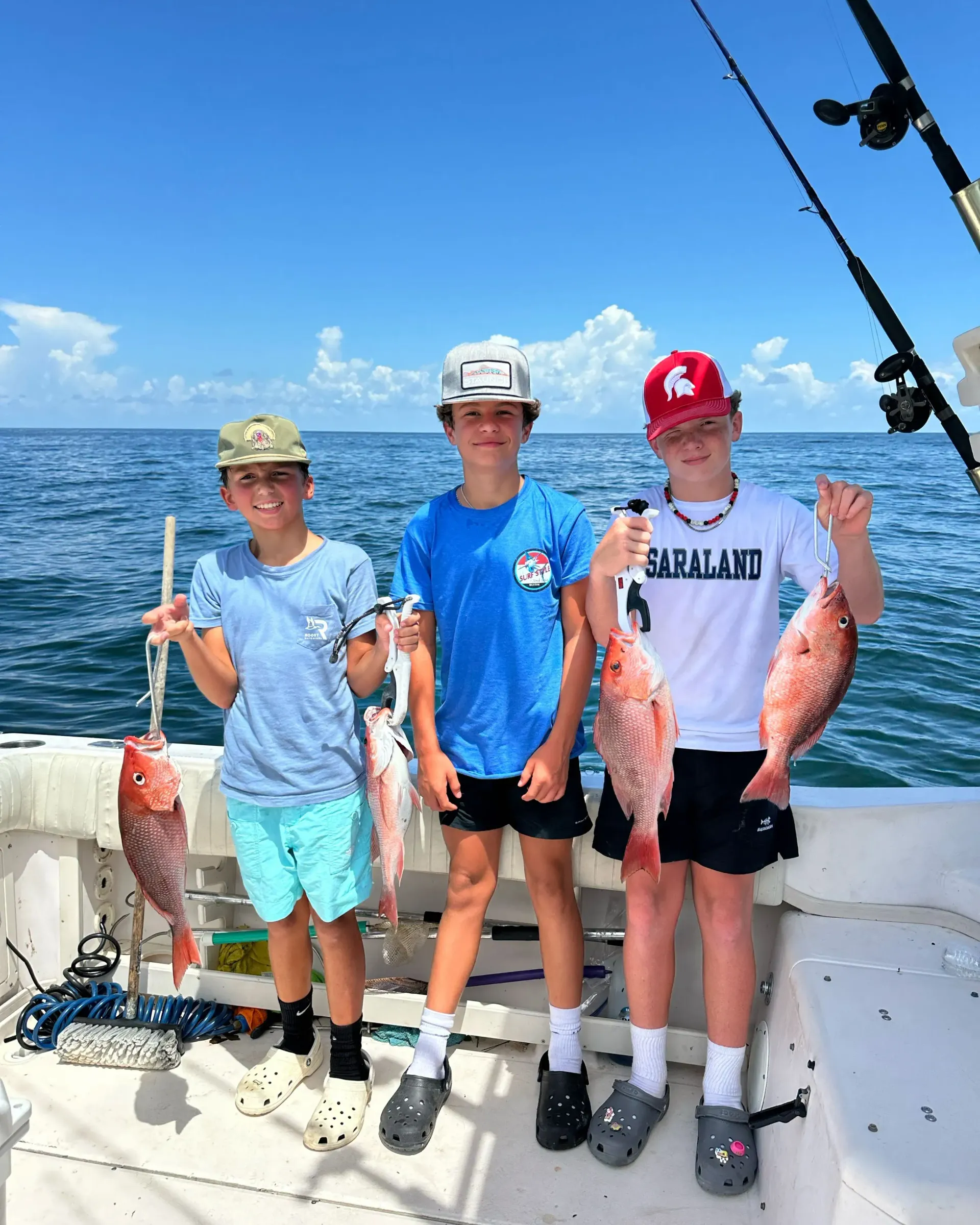 Three young boys are standing on a boat holding fish.