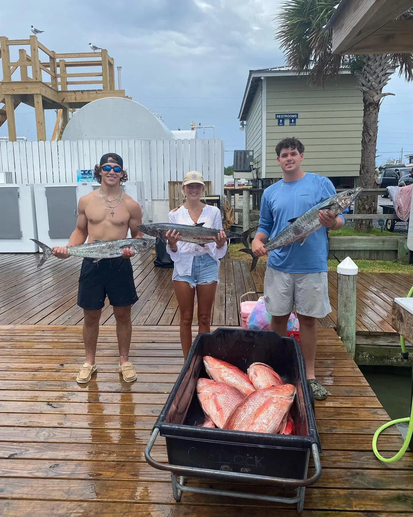 Three people are standing on a dock holding fish.