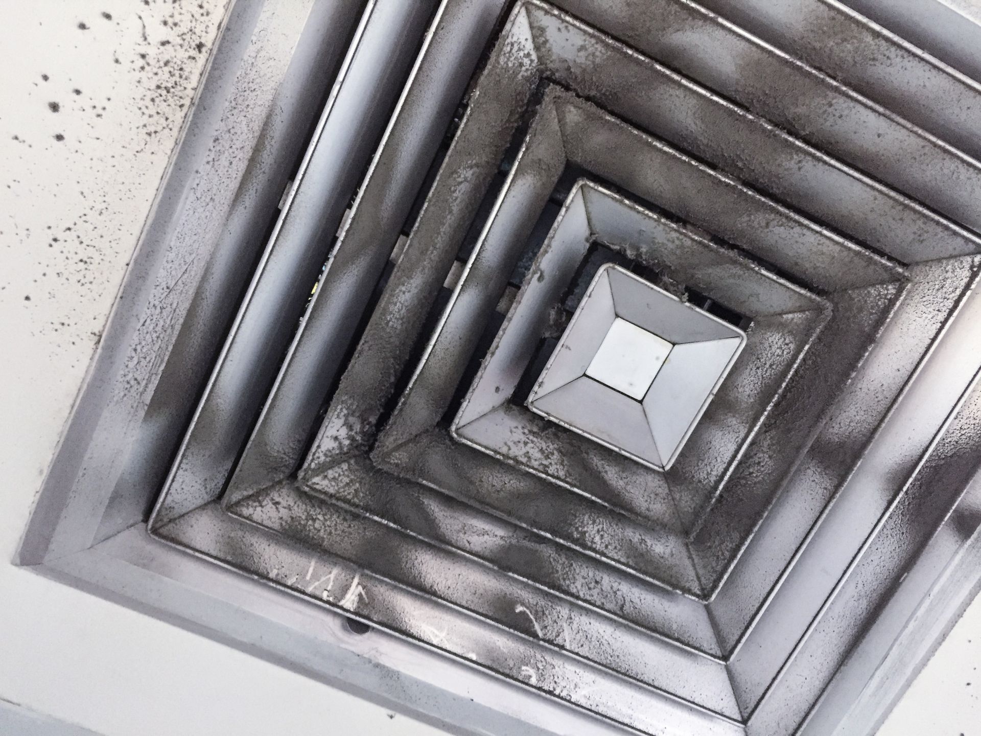 Geometric metal stairwell viewed upward, with gray concentric square frames around a central skylight.
