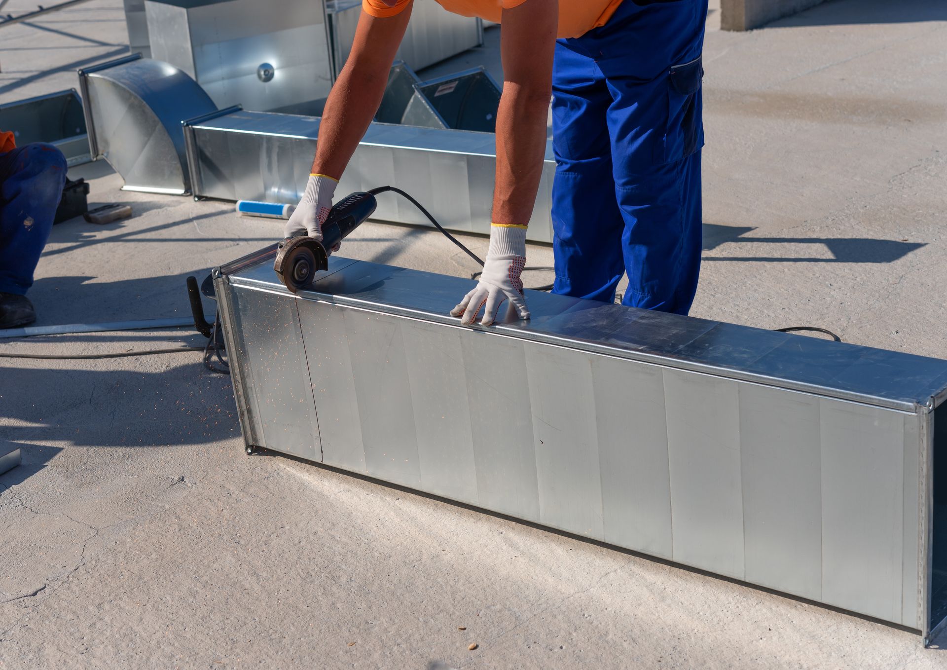 Workers loading a long metal panel onto a rooftop, with blue protective gear visible.