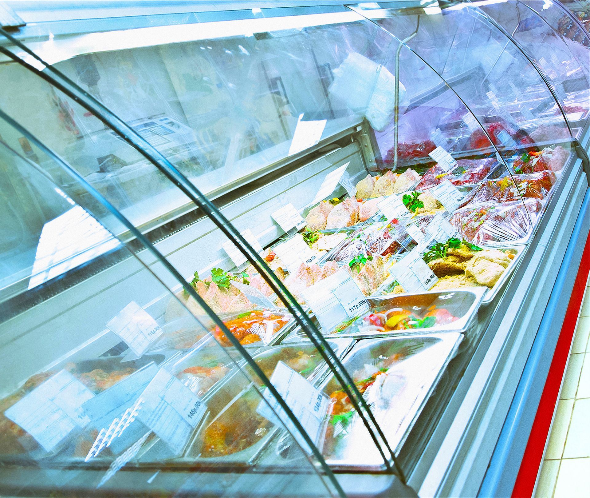 Curved deli display case with assorted meats, cheeses, and prepared foods in a bright store