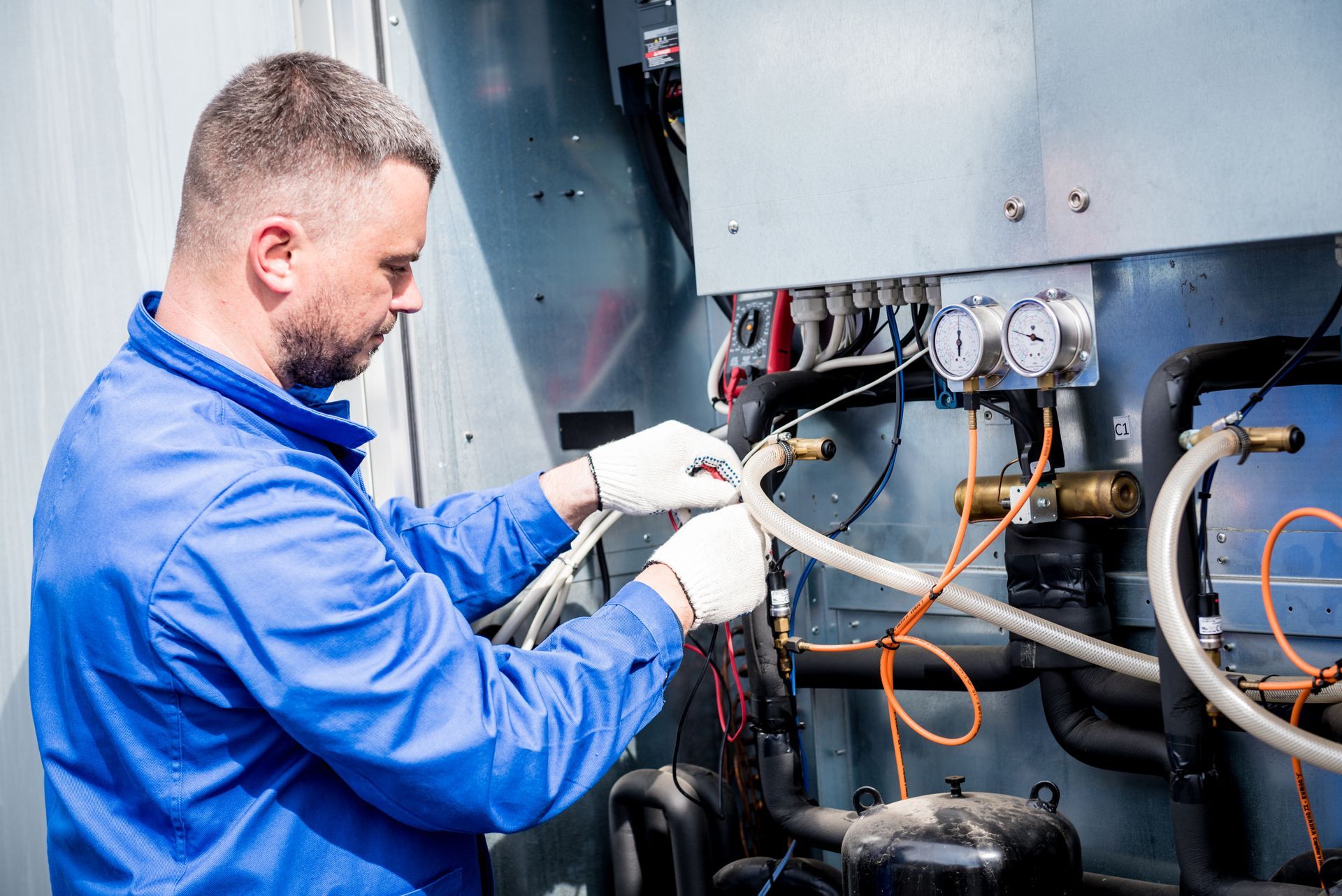 Technician in blue coveralls repairs HVAC unit with tools and wiring
