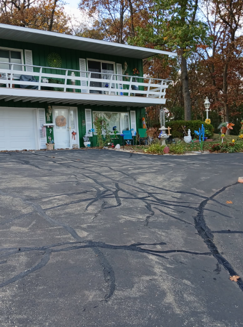 House under construction with two-car garage; workers compacting gravel driveway on a sunny day.