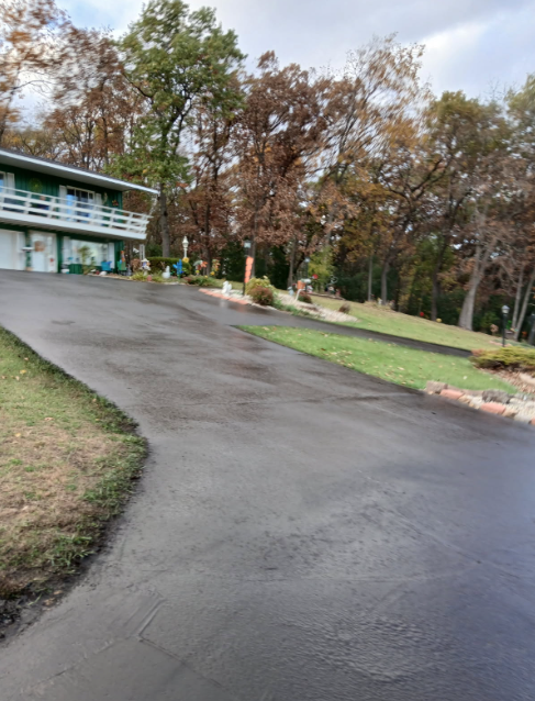 New asphalt driveway leading to a gray house with a red door and two-car garage; a person is working on the driveway.