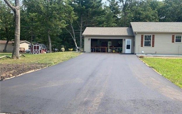 Newly paved asphalt driveway leading to a garage, residential house, green lawn, trees, sunny.