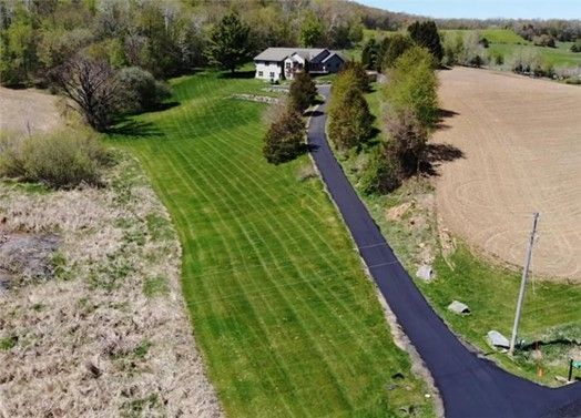 Aerial view of a house with a long driveway, green lawn, and fields.