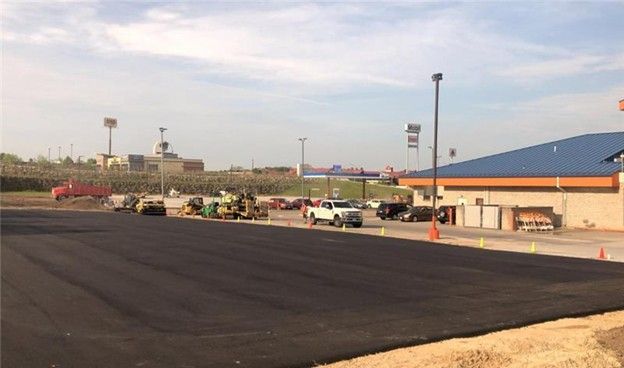 New asphalt parking lot with construction vehicles near a building and distant buildings on a sunny day.