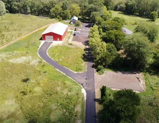 Aerial view of a red barn with a paved driveway winding through green fields and trees.