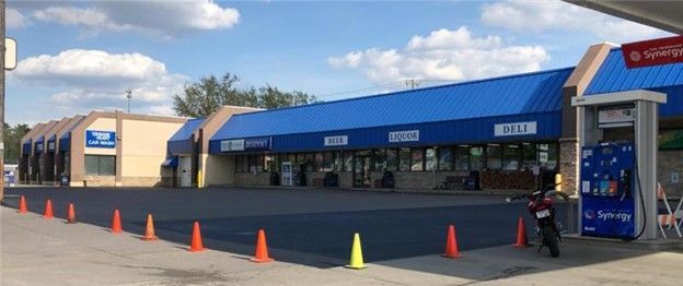 Exterior of a convenience store with gas pumps and a blue roof. Orange and yellow cones line the parking lot.