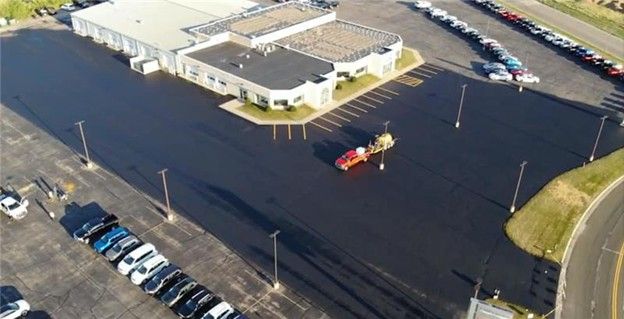 Aerial view: car dealership with rows of cars, a red truck, and paved parking area.