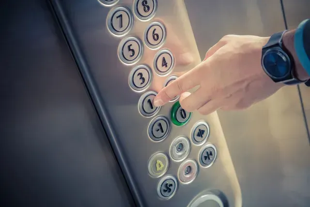 Mano presionando un panel de botones de ascensor iluminado con botones de piso numerados