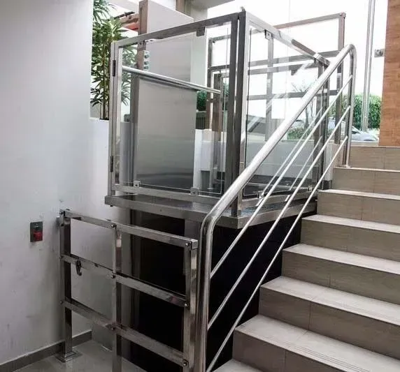 Plataforma de ascensor con barandillas metálicas junto a una escalera en el pasillo de un edificio.