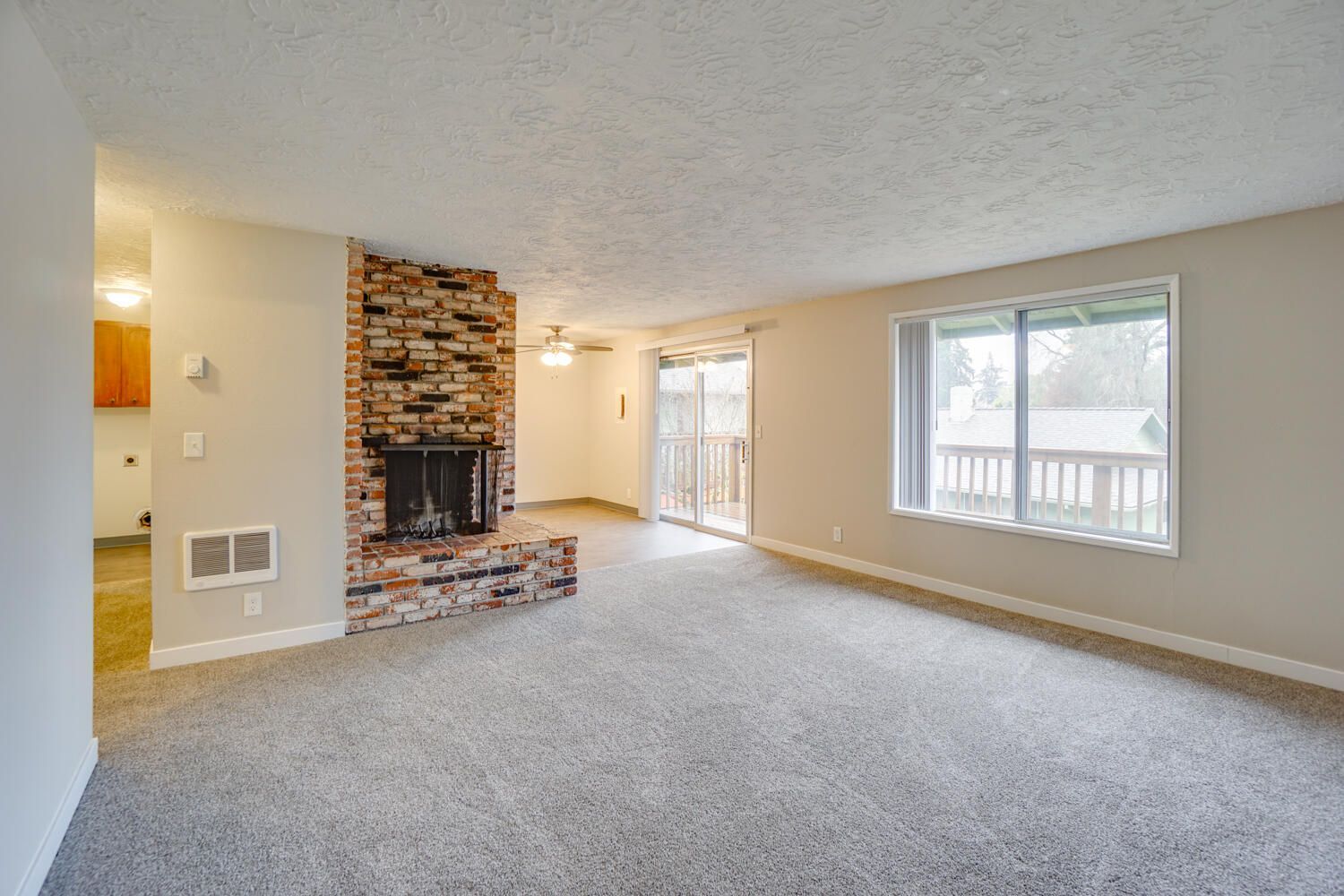 An empty living room with a fireplace and sliding glass doors.