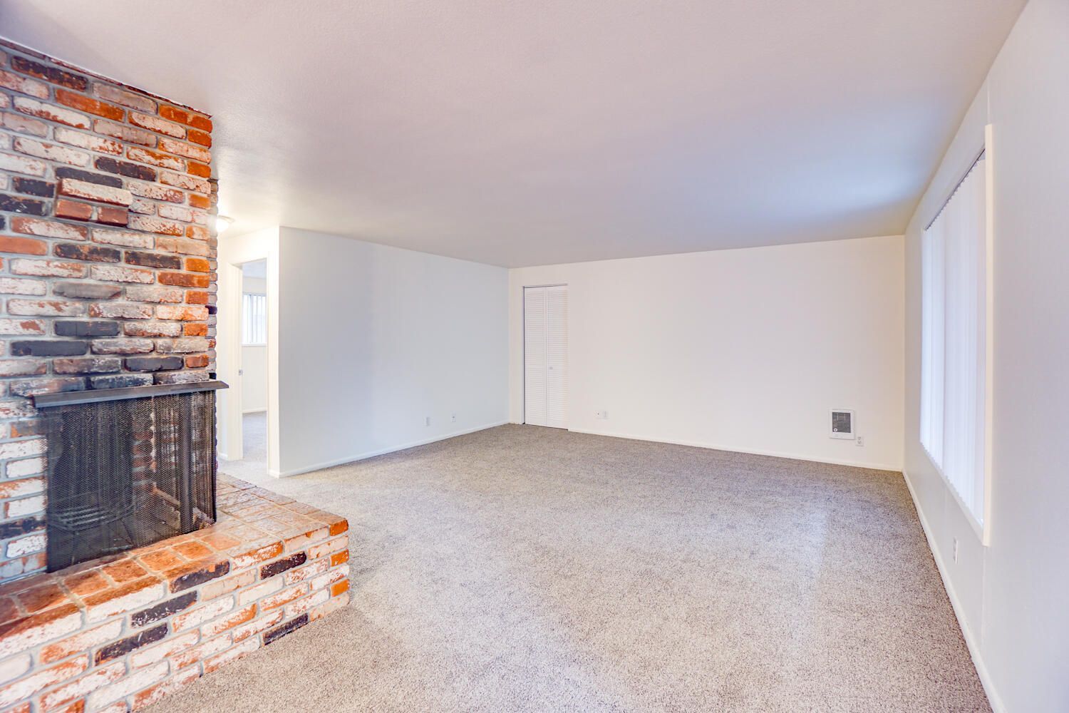An empty living room with a brick fireplace and carpet.