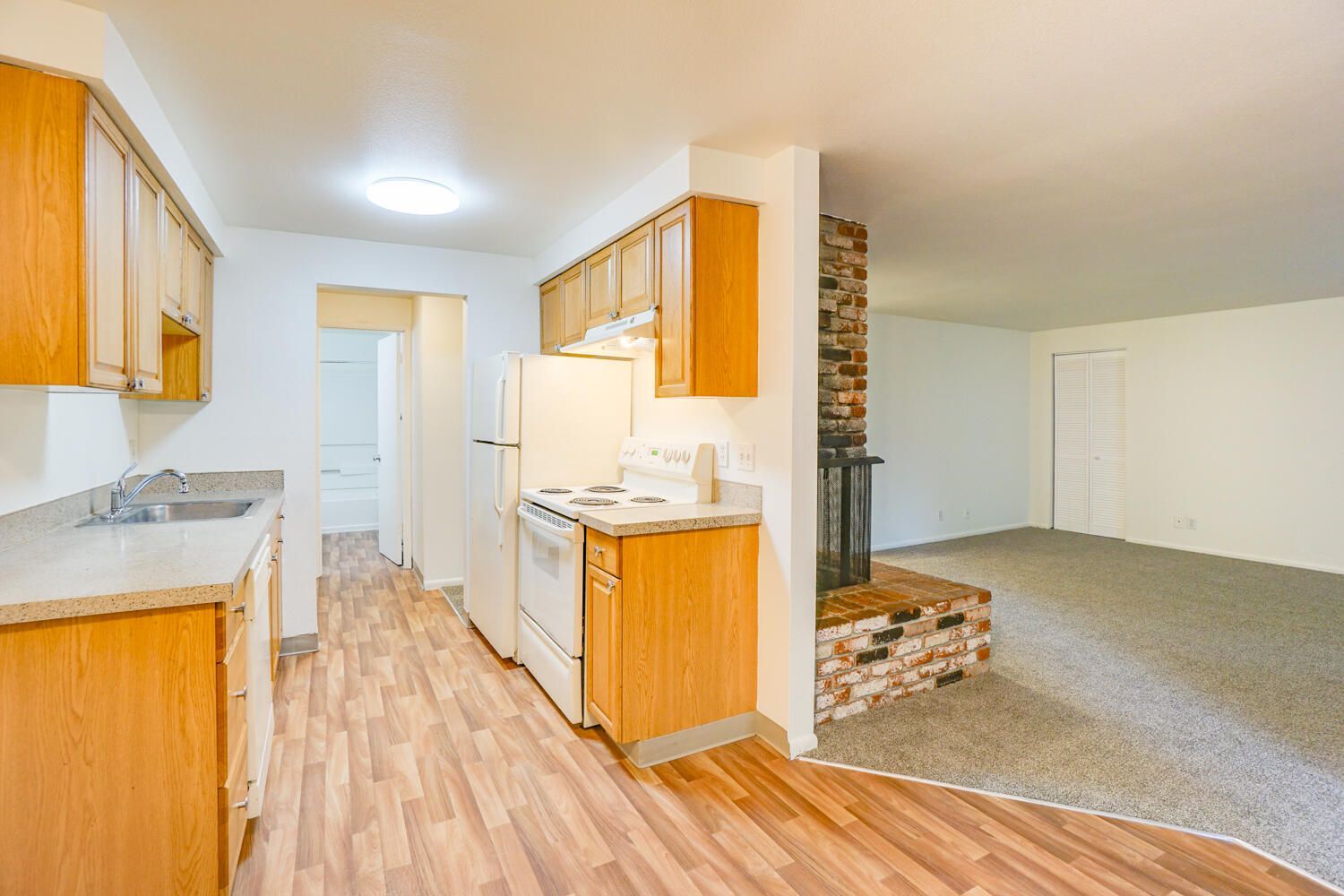 A kitchen with wooden cabinets , a refrigerator , stove , sink and fireplace.