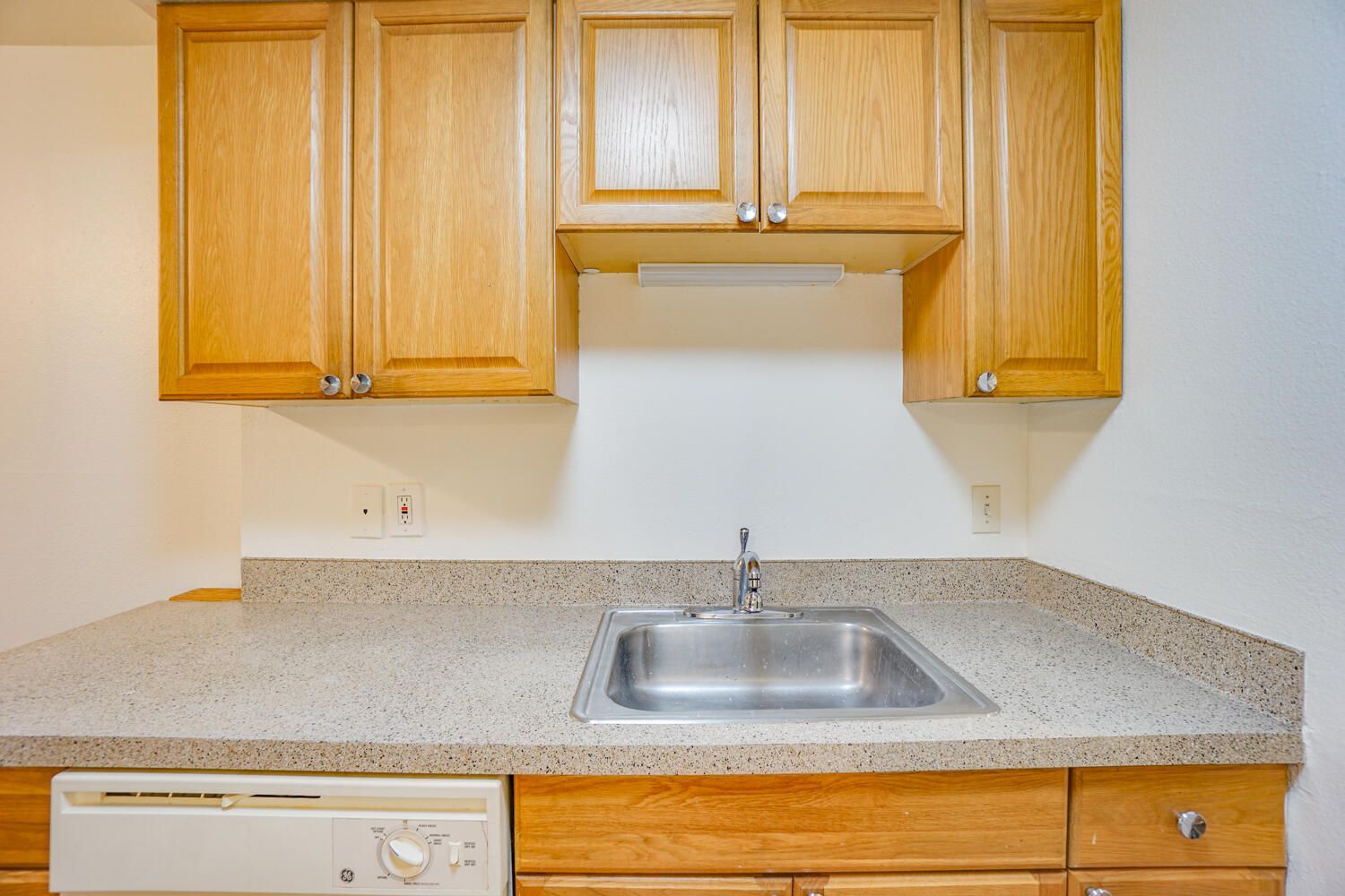 A kitchen with a sink , dishwasher , and wooden cabinets.