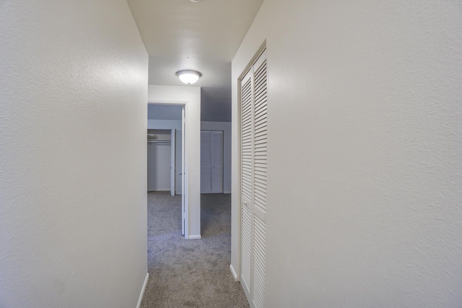 A hallway in a house with white walls and a closet.
