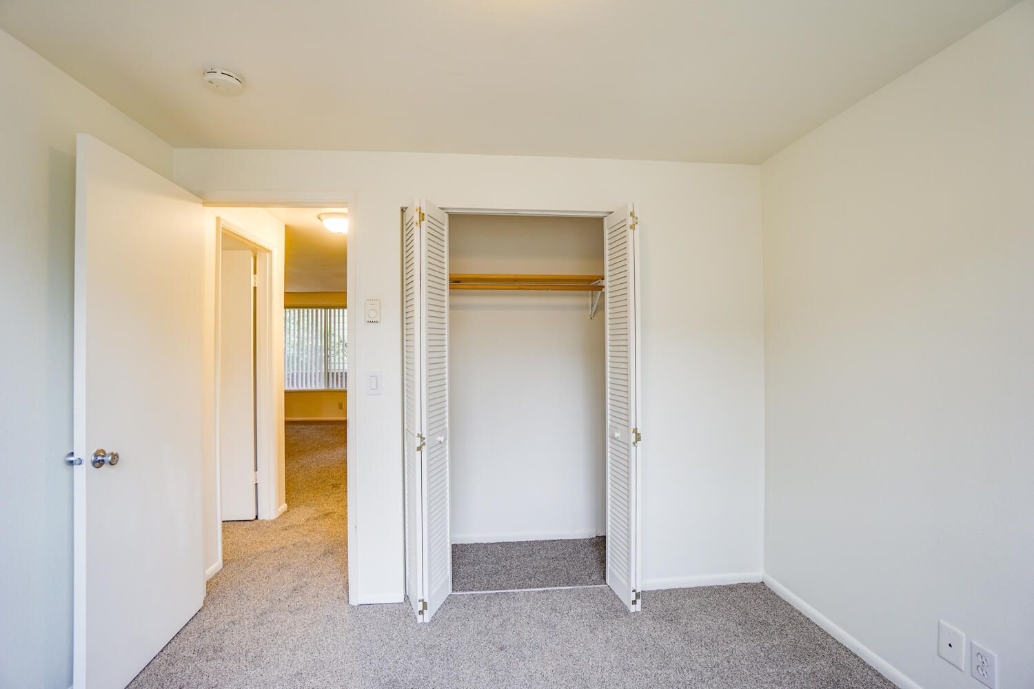 An empty bedroom with two closets and a carpeted floor.