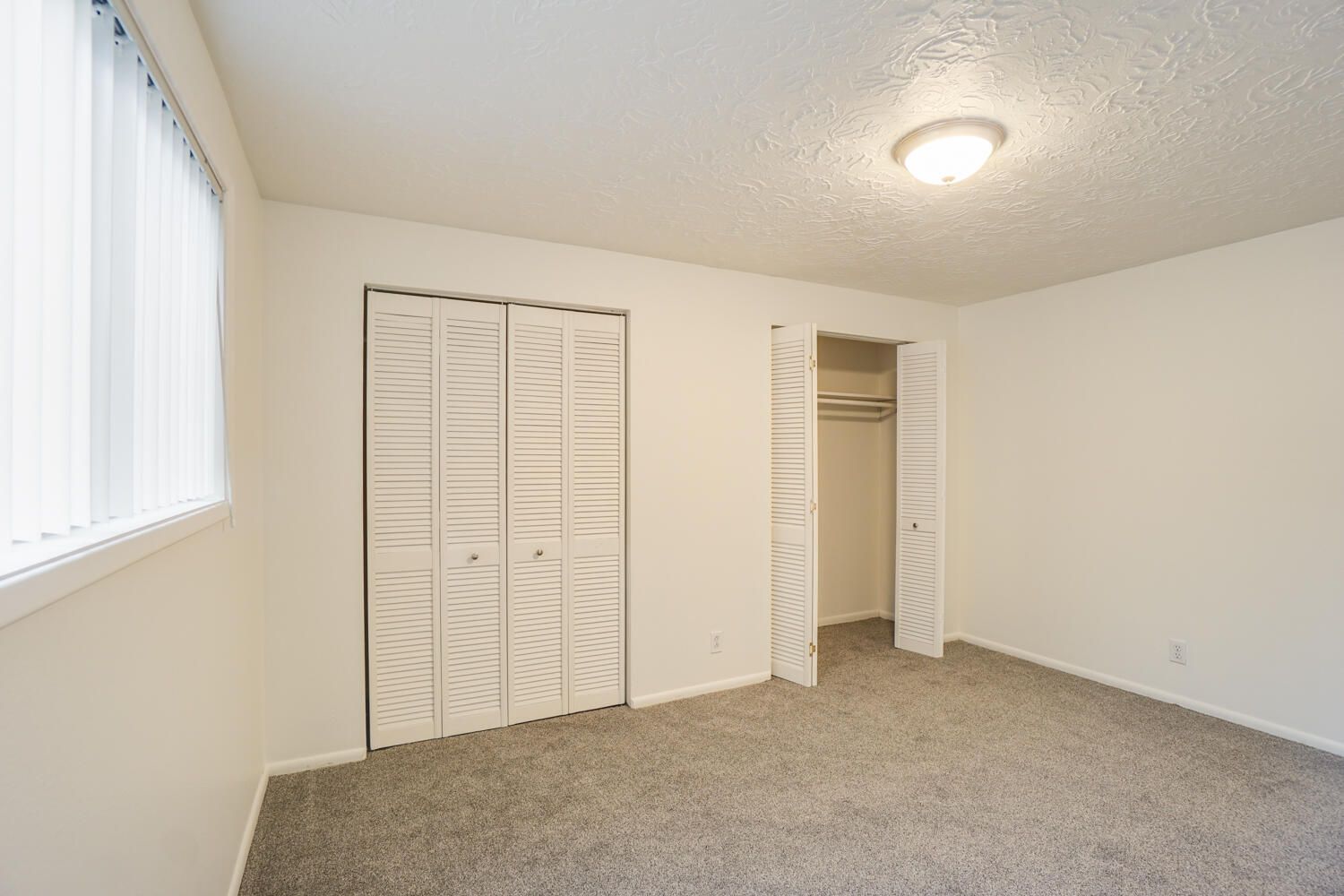 An empty bedroom with a closet and a window.