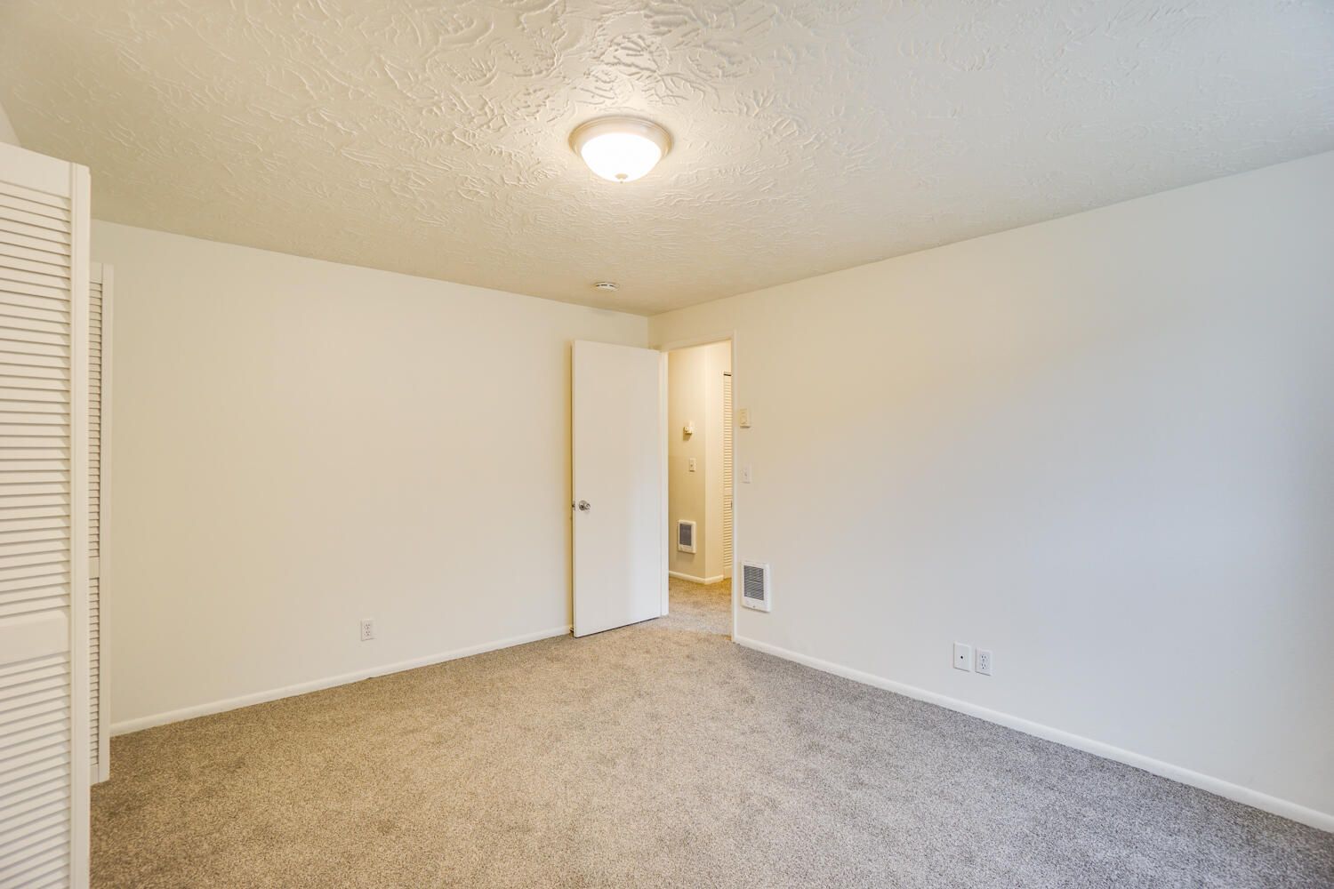An empty bedroom with a carpeted floor and white walls.