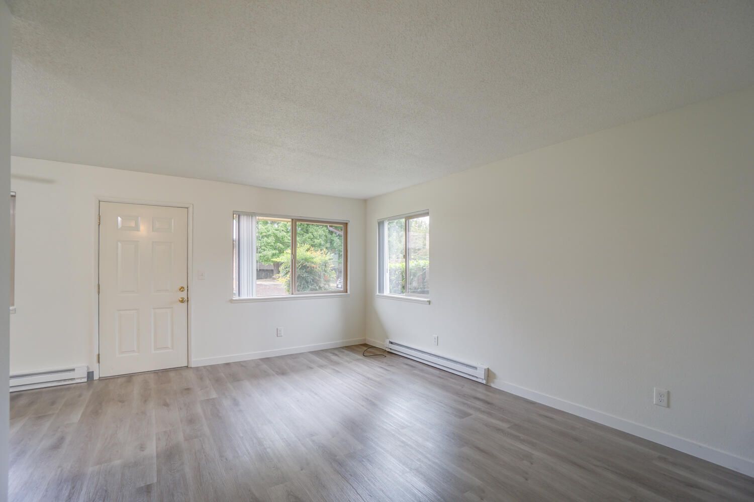 An empty living room with hardwood floors and white walls.