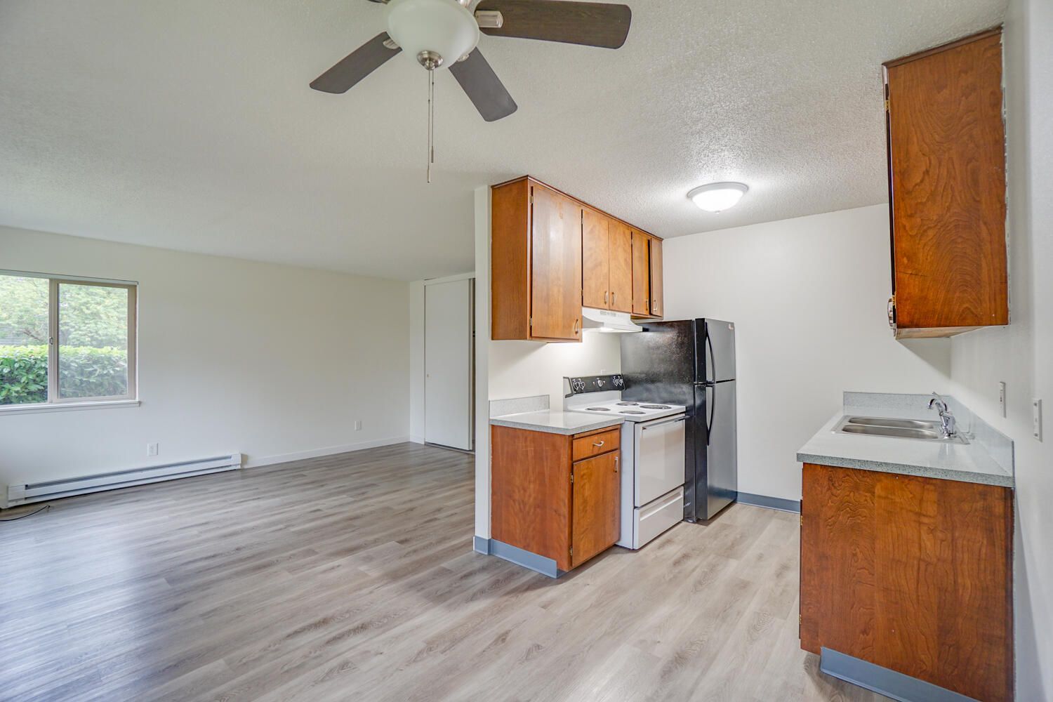 A kitchen with wooden cabinets , a refrigerator , a stove , and a ceiling fan.