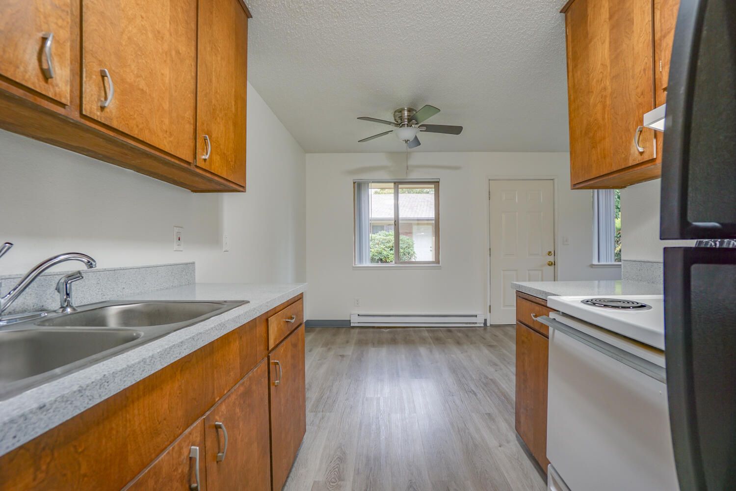 A kitchen with wooden cabinets , a sink , a refrigerator , and a ceiling fan.