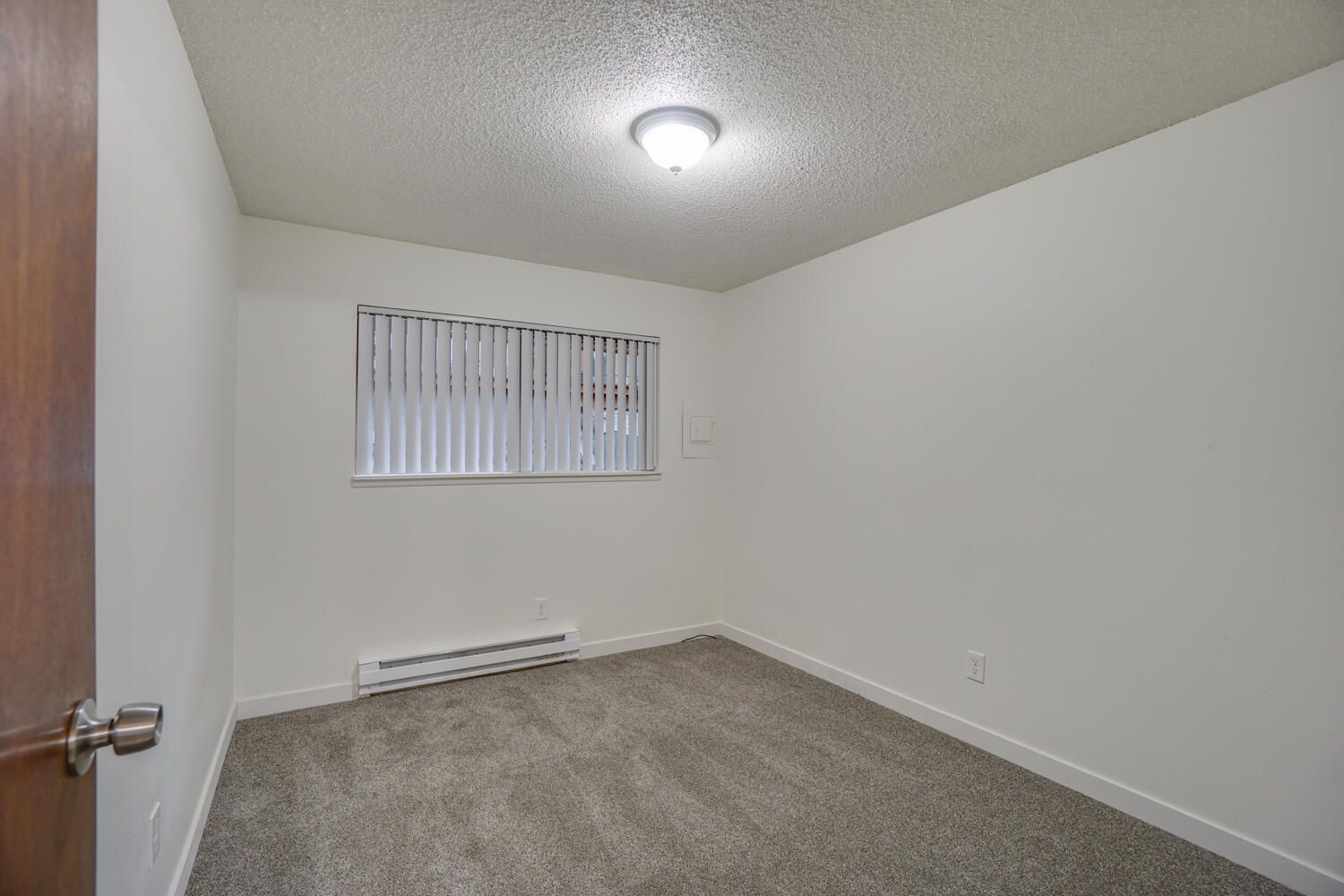 An empty bedroom with a window and a ceiling light.