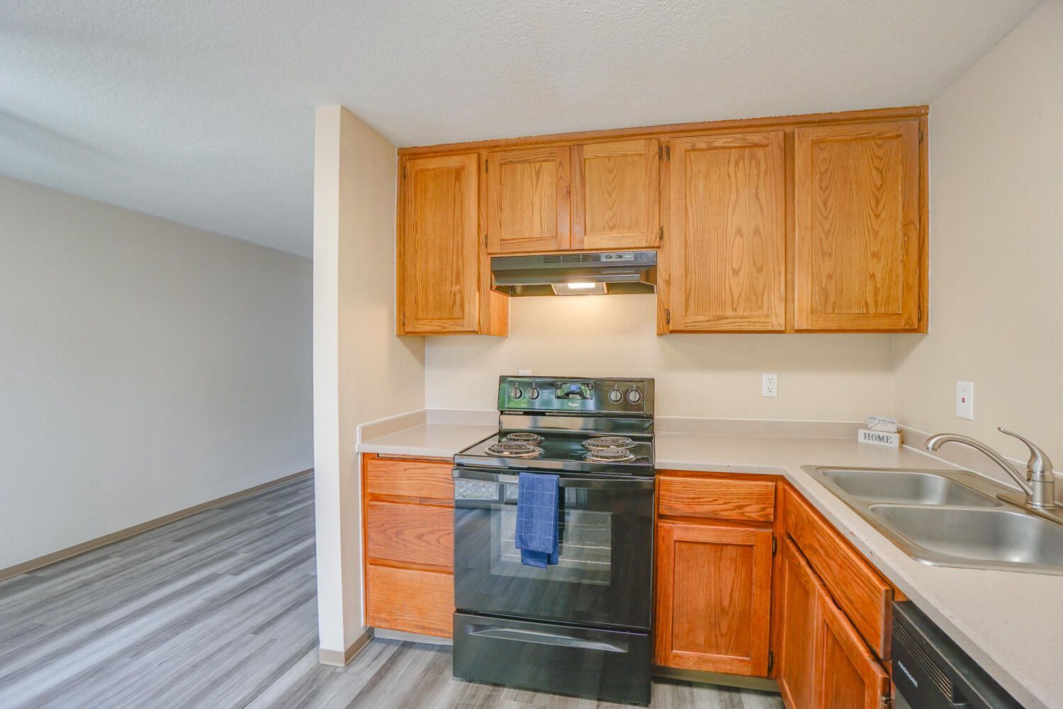 A kitchen with wooden cabinets , a stove , a sink , and a dishwasher.
