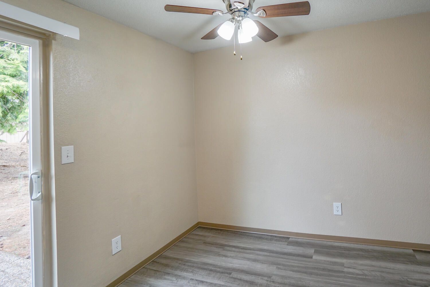 An empty room with a ceiling fan and a sliding glass door.