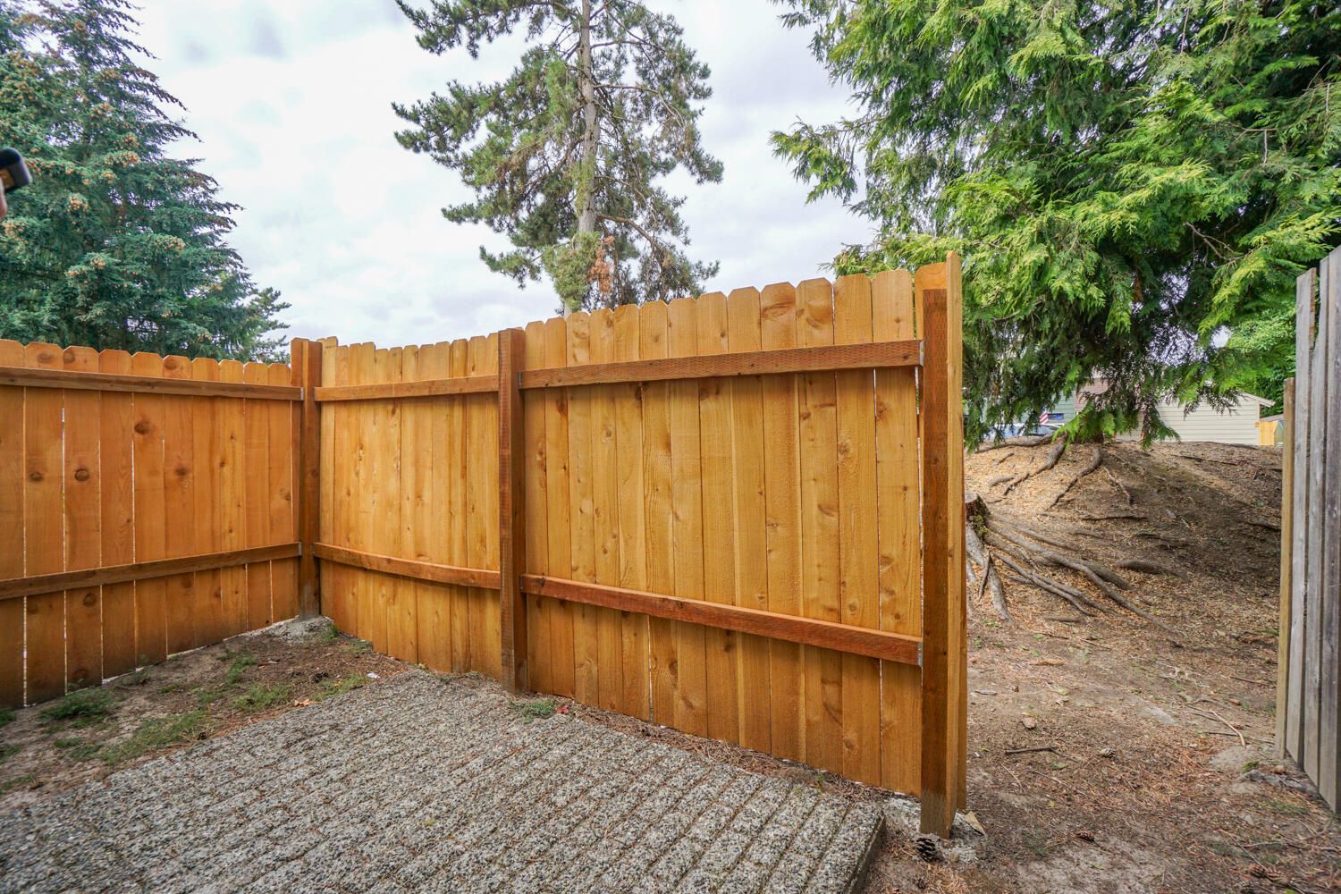 A wooden fence is surrounded by gravel and trees.