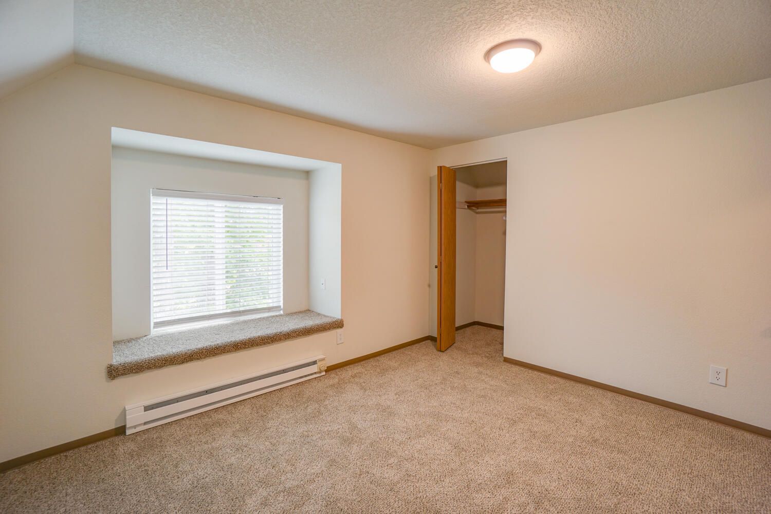 An empty bedroom with a window and a closet.