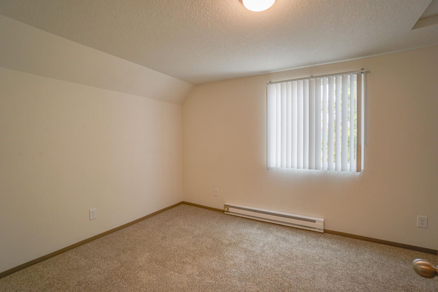 An empty bedroom with a window and blinds.