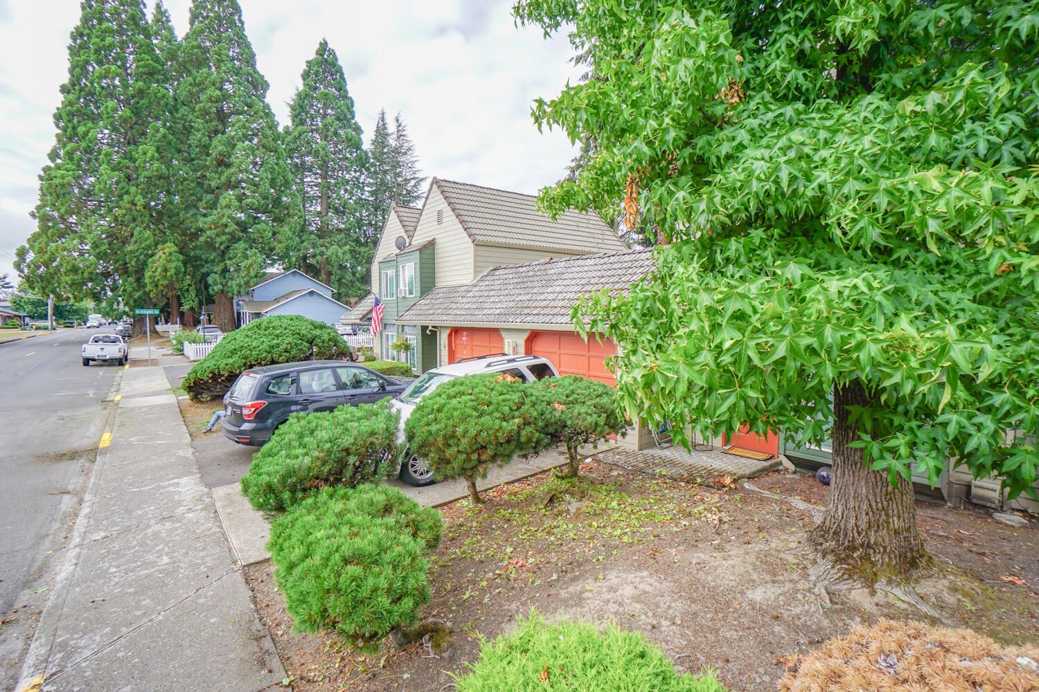 A house with a red garage door is surrounded by trees and bushes.