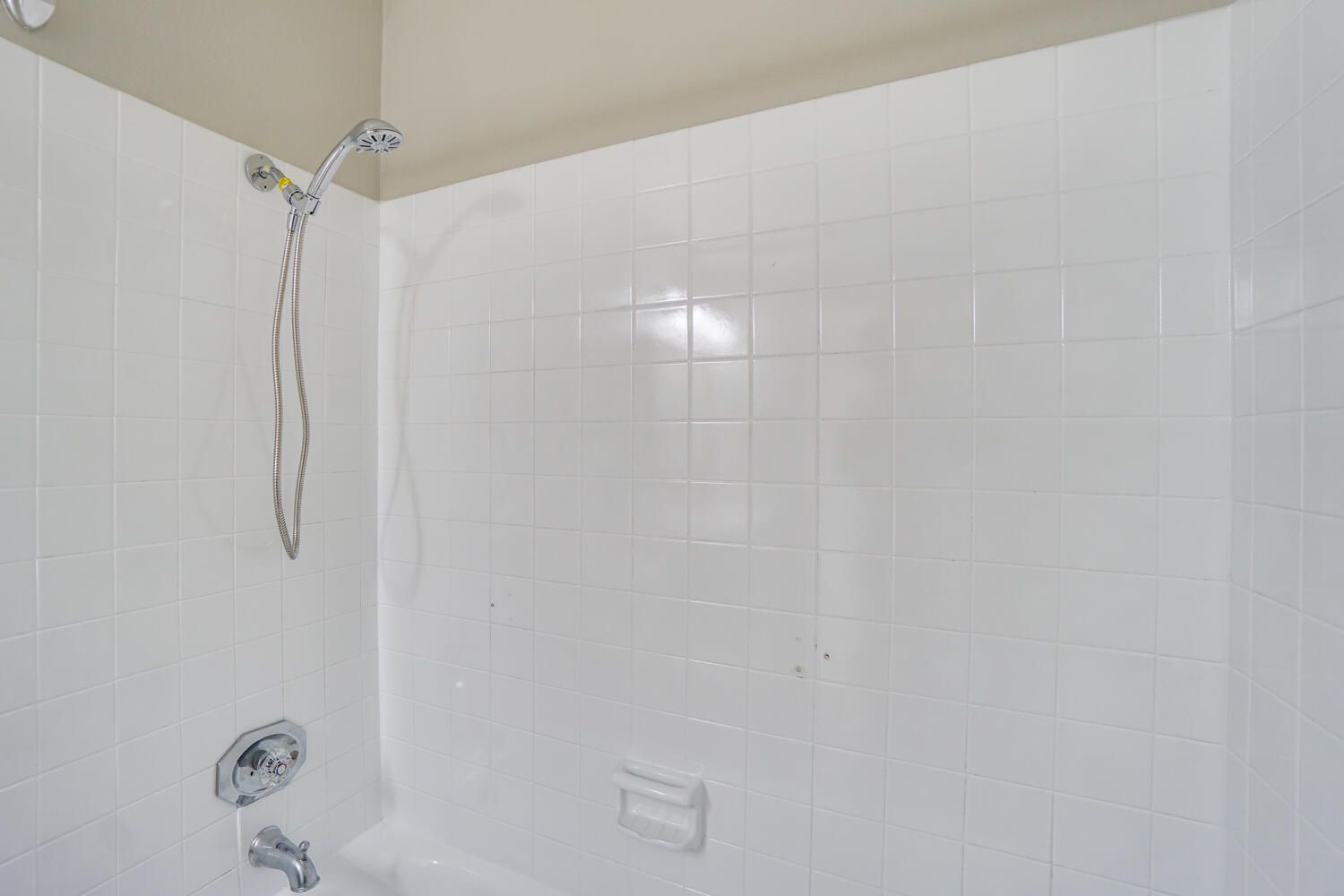 A bathroom with white tiles and a shower head.