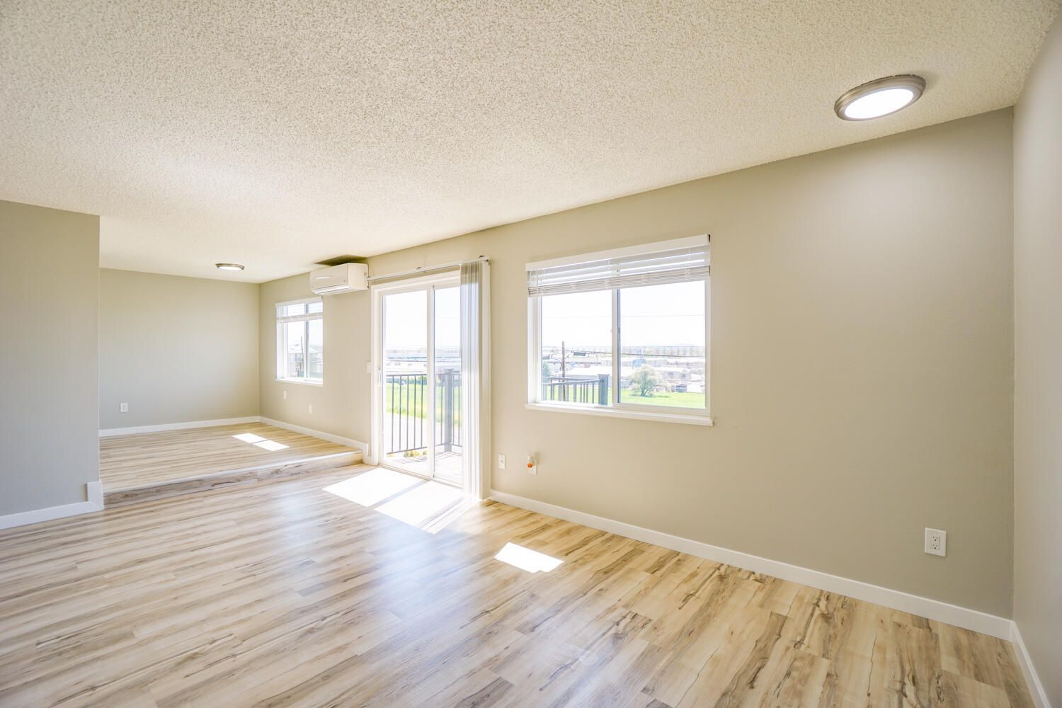 An empty living room with hardwood floors and sliding glass doors.