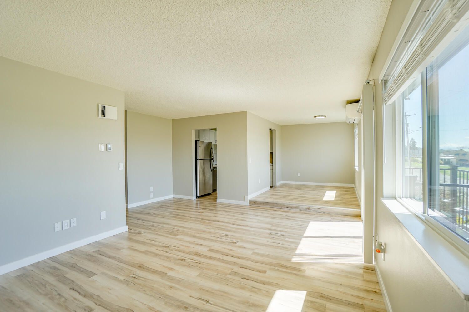 An empty living room with hardwood floors and a refrigerator.