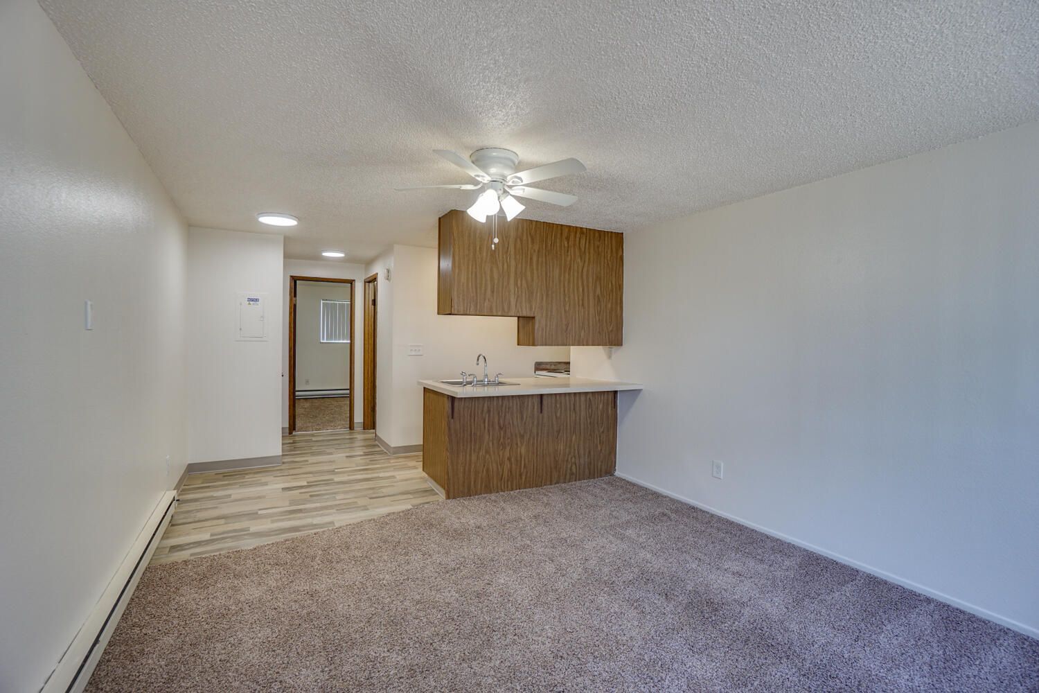 A living room with a ceiling fan and a kitchen in the background.
