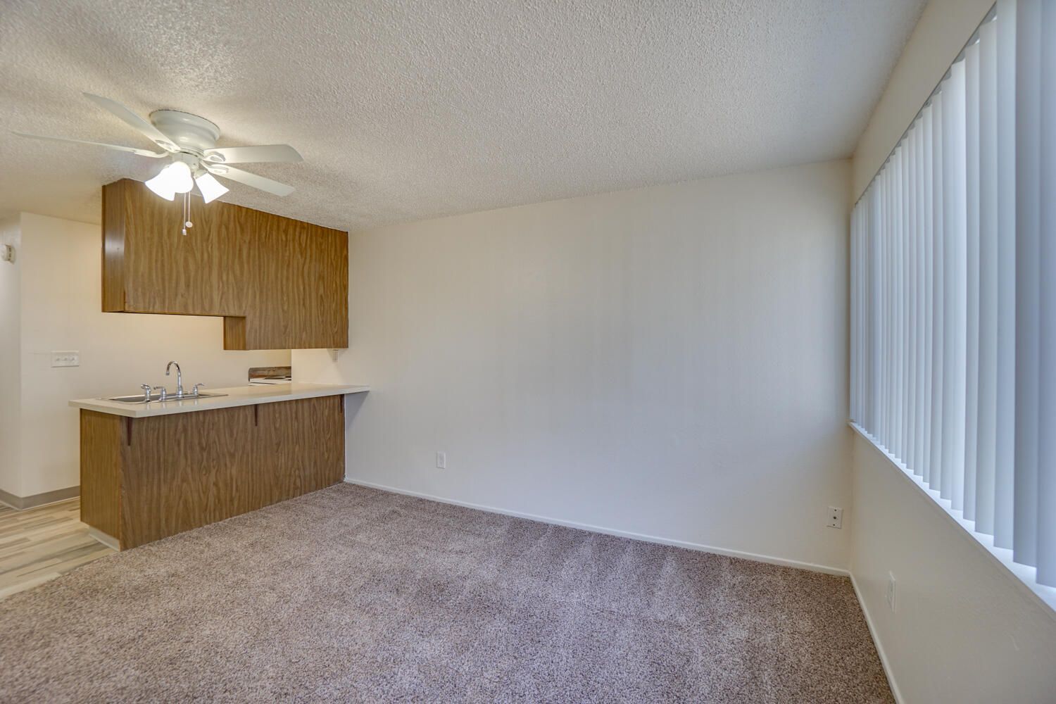 A living room with a ceiling fan and a kitchen in the background.
