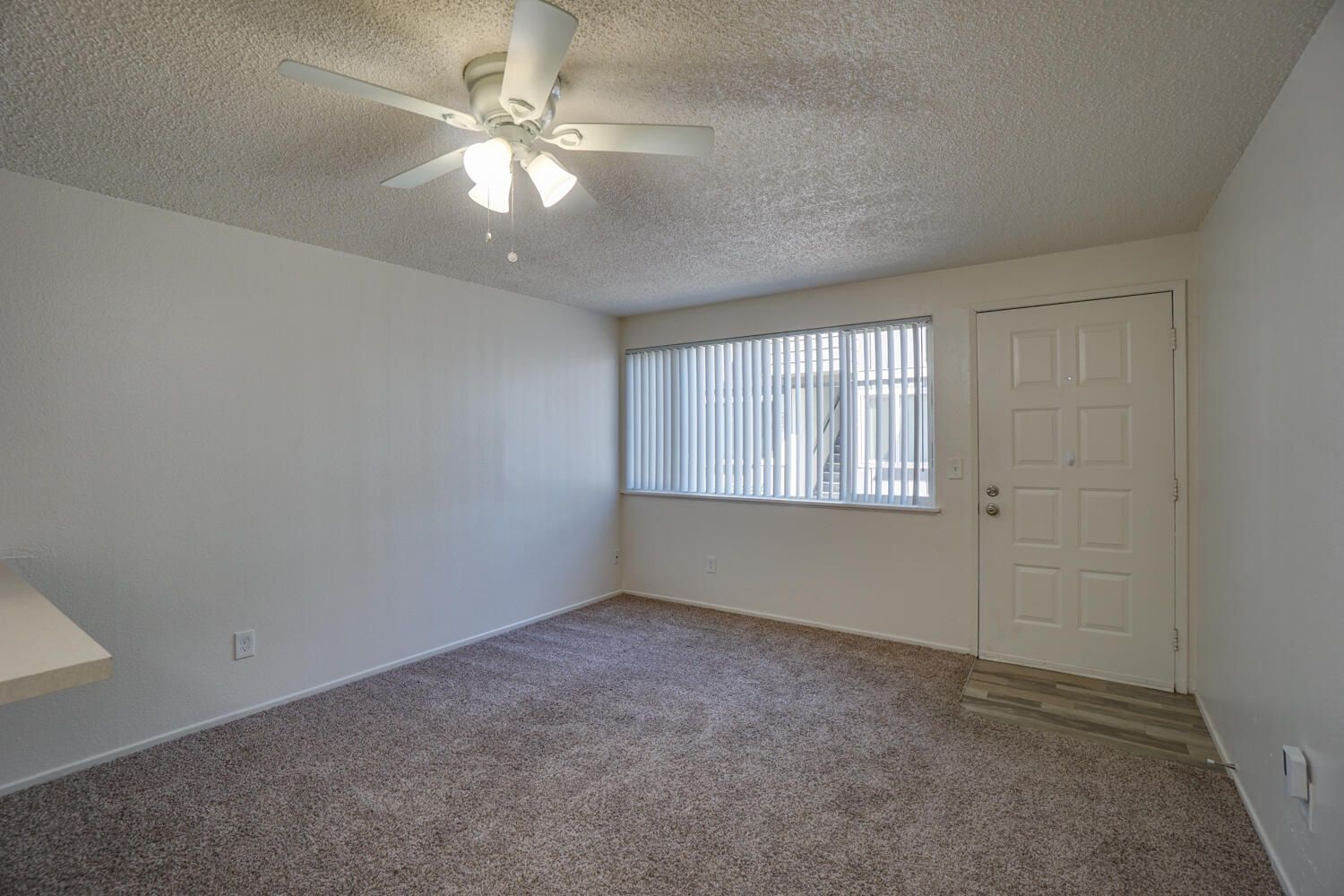An empty living room with a ceiling fan and a window.