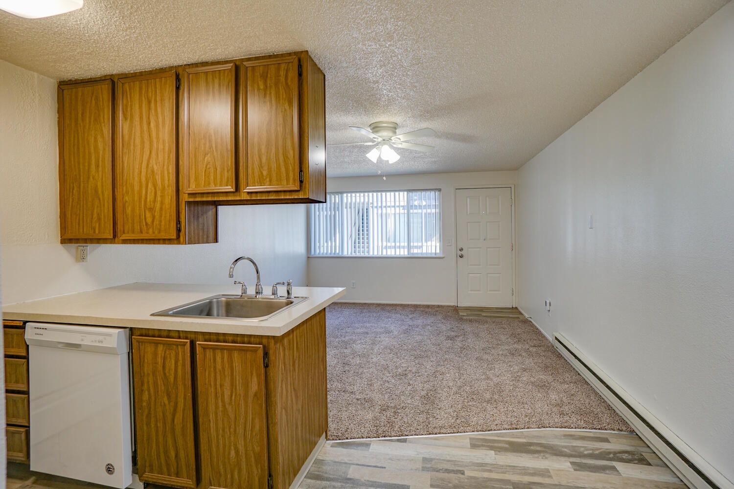 An empty kitchen with wooden cabinets , a sink , and a dishwasher.